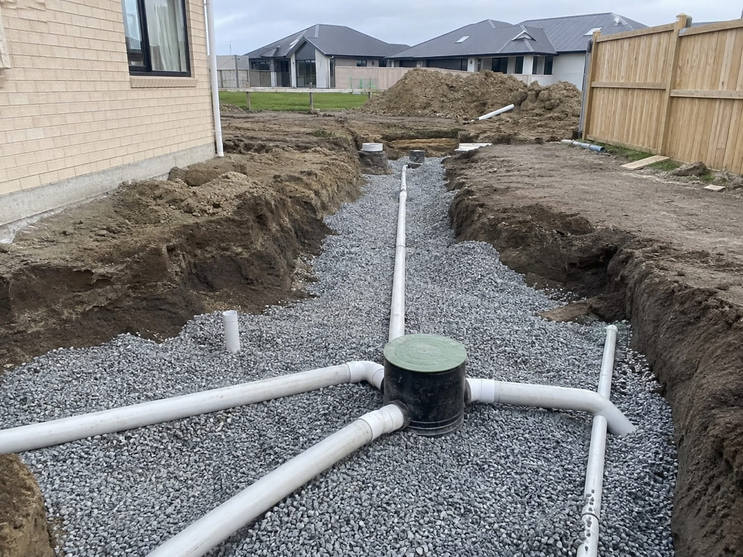 Stormwater junction chamber and branching pipe network bedded in gravel across a Christchurch subdivision