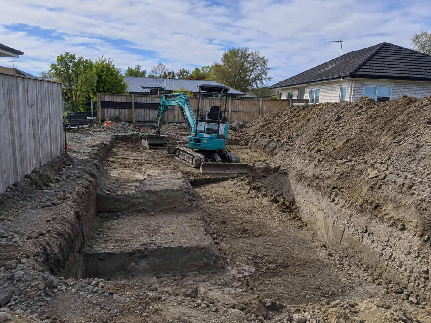 Excavator digging foundation trenches beside a Christchurch home